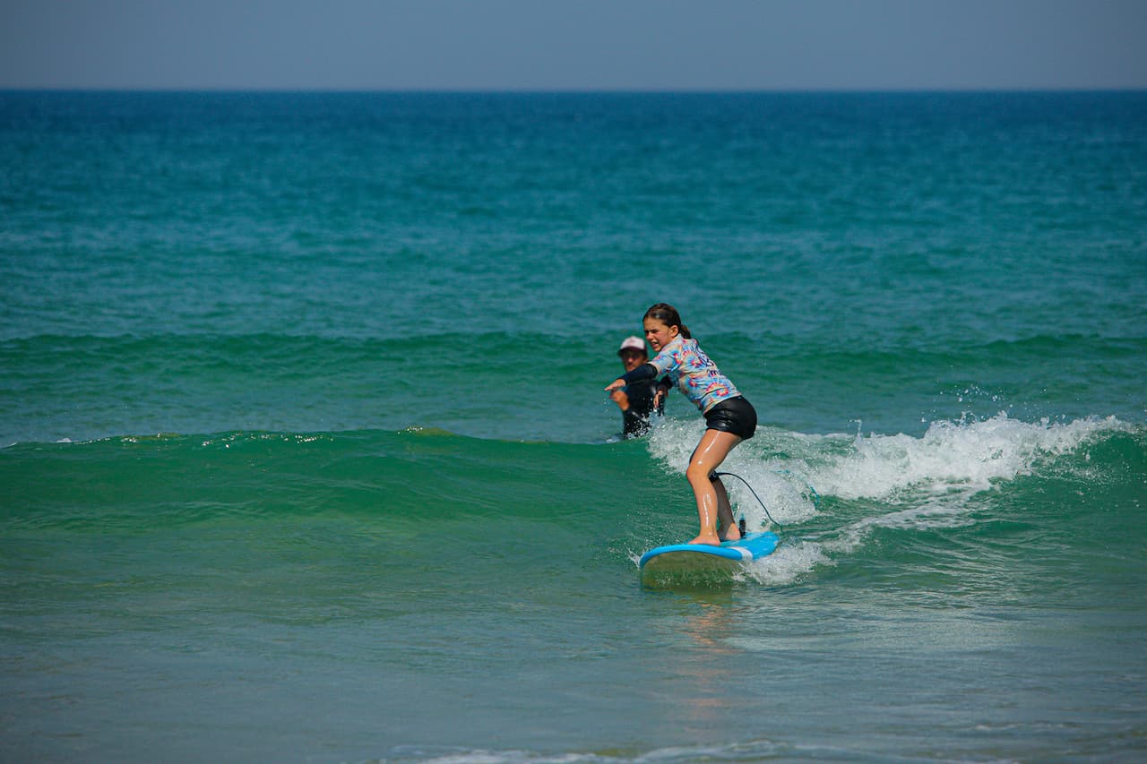 Une fillette surfant une petite vague à Lacanau surveillée par son moniteur