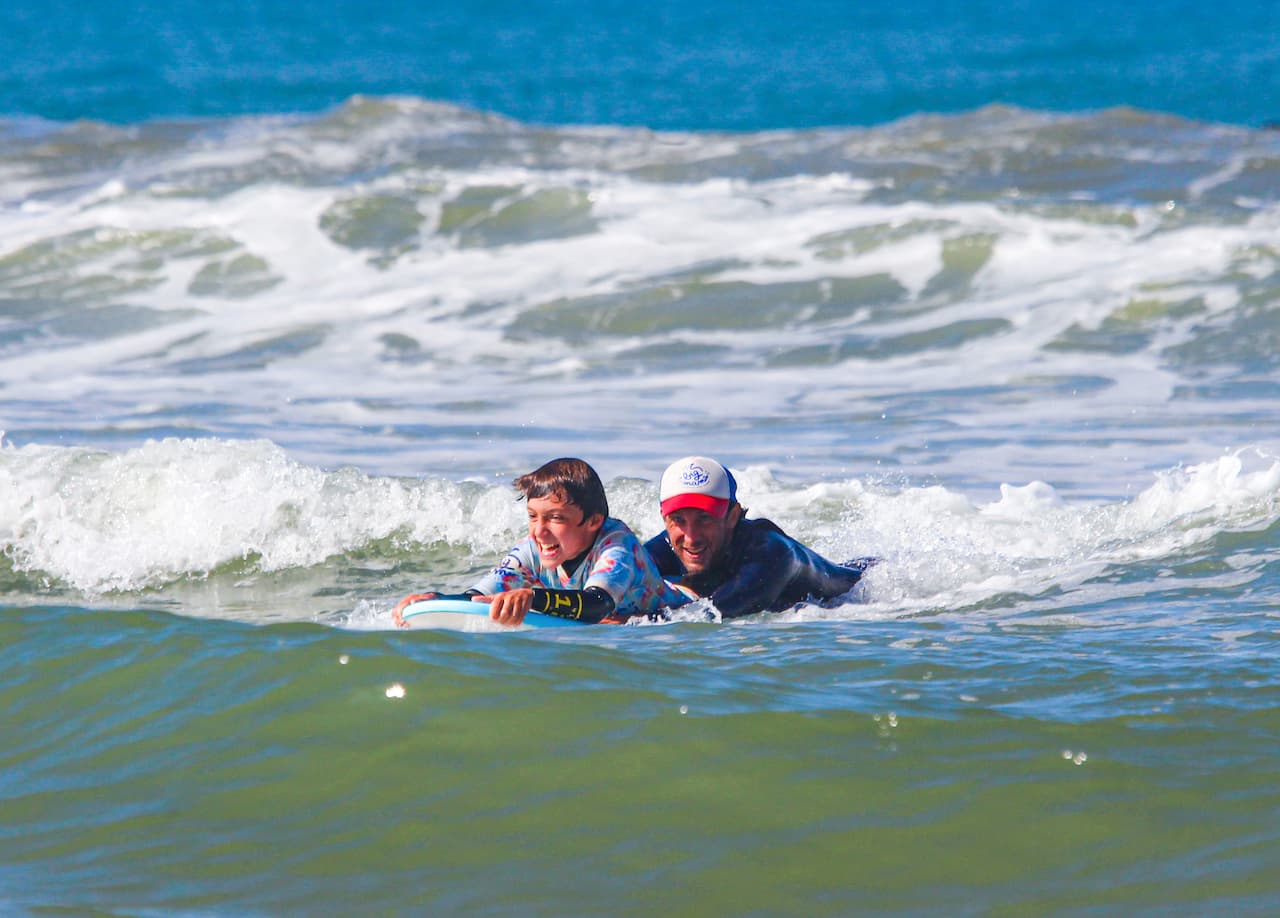 Un jeune surfeur et son moniteur sur la même planche durant un cours particulier à Lacanau
