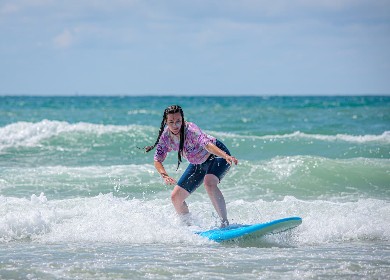 Une surfeuse débutante très concentrée sur sa position sur la planche pendant un cours d'initiation au surf à Lacanau