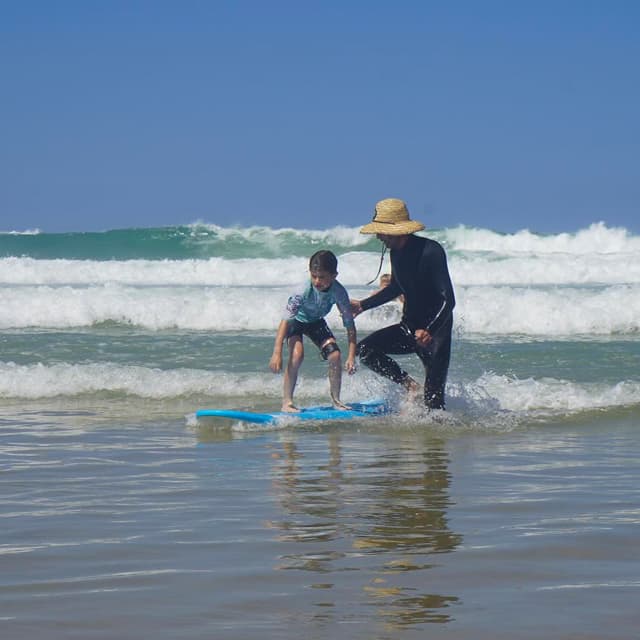 Petit garçon debout sur sa planche avec son moniteur de surf à Lacanau